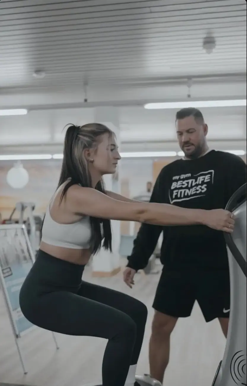 Trainer unterstützt Mitglied an einem Trainingsgerät