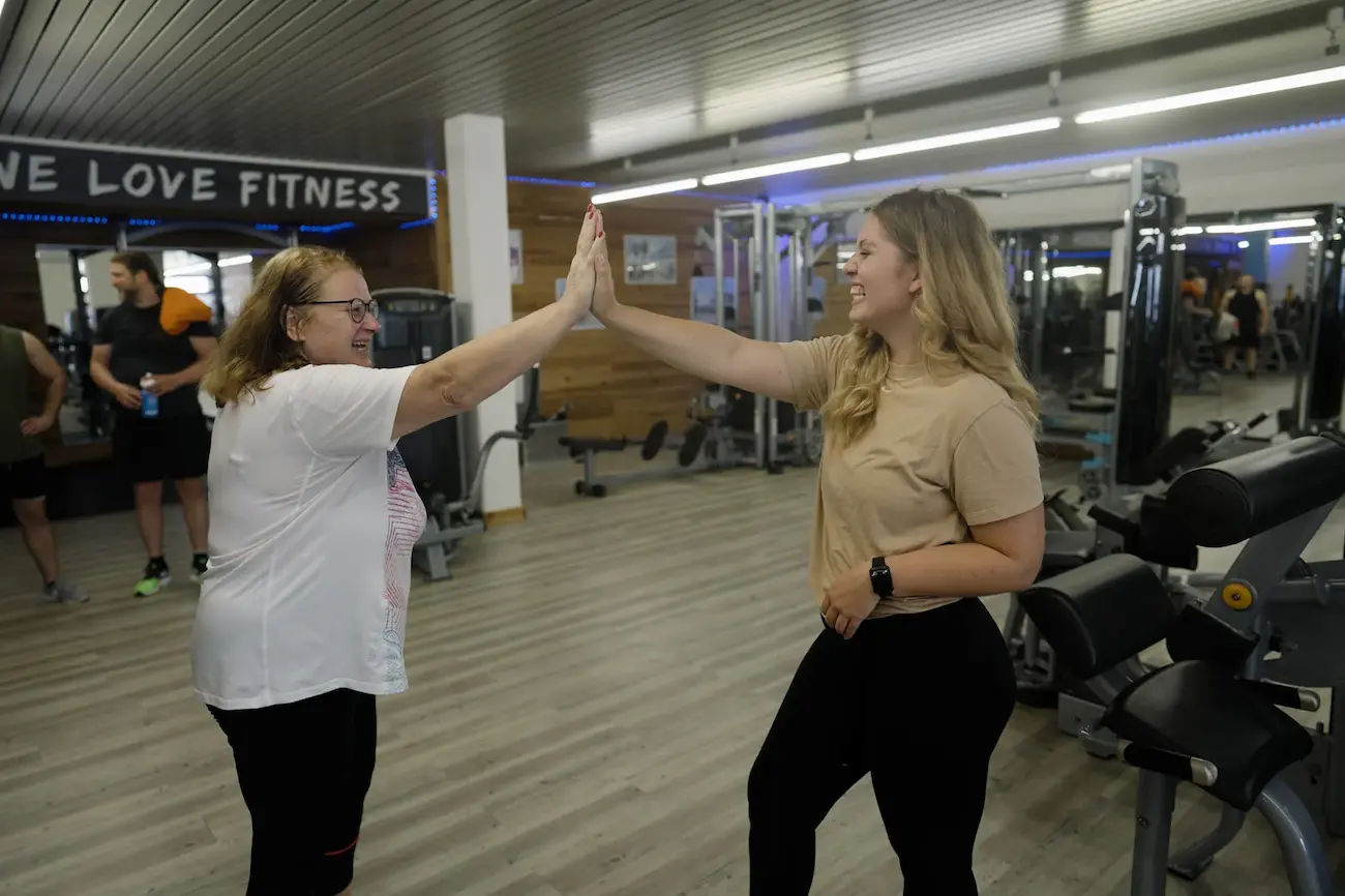 Zwei Mitglieder geben sich lachend ein High-Five vor dem „We Love Fitness“-Schriftzug