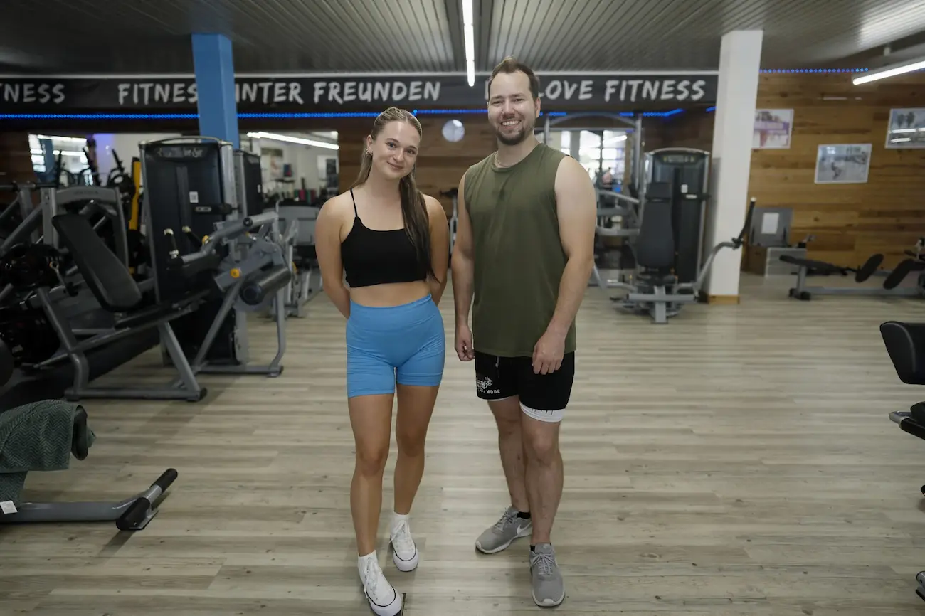 Zwei Mitglieder stehen lächelnd unter dem Schriftzug „Fitness unter Freunden“