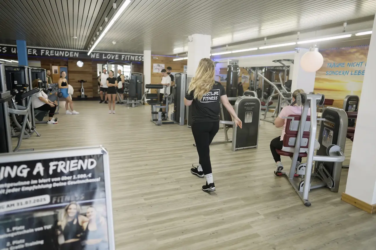 Trainerin im BestLife-Fitness-Shirt geht durch den Trainingsbereich