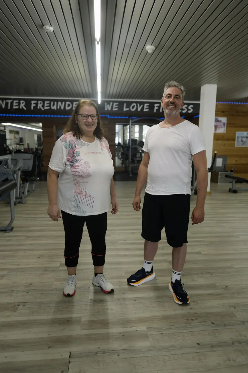 Zwei Mitglieder stehen lächelnd unter dem Schriftzug „We Love Fitness“